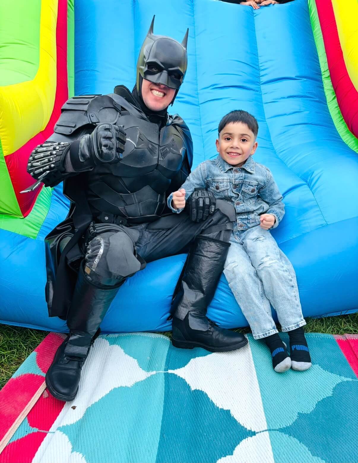 Dark-caped superhero entertainer with a child at a birthday celebration